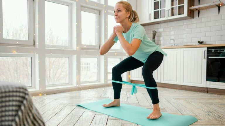woman performing bodyweight squat exercise at home using resistance band for strength training