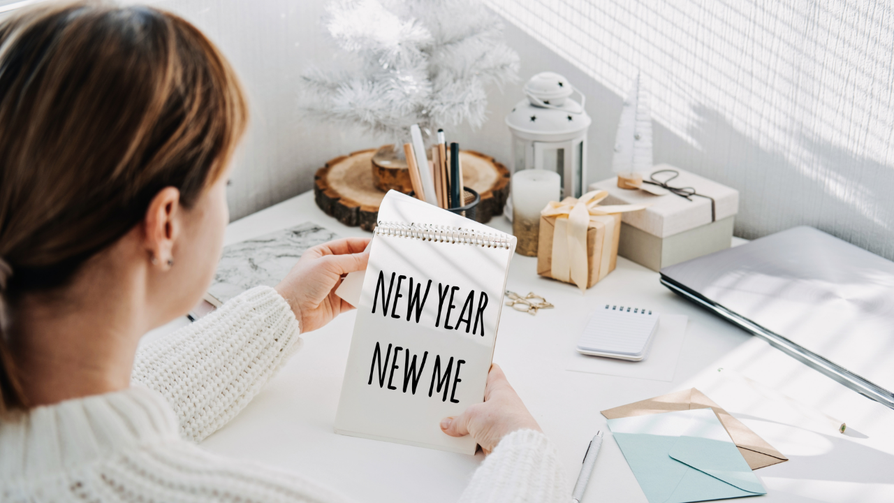 woman holding a notepad that reads “New Year New Me” at a desk with winter decor, symbolizing goal setting and fresh starts